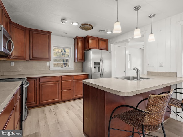 kitchen featuring a sink, stainless steel appliances, light wood-style floors, a peninsula, and a breakfast bar area