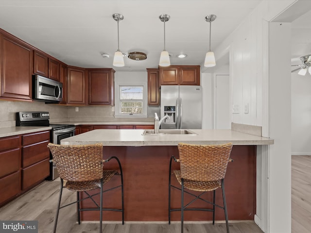 kitchen with a kitchen bar, a sink, decorative light fixtures, stainless steel appliances, and light wood finished floors