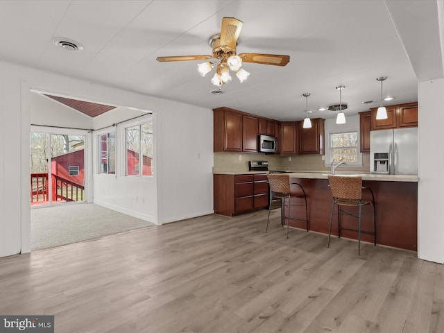 kitchen with a kitchen breakfast bar, appliances with stainless steel finishes, light wood-style flooring, and light countertops