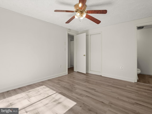 unfurnished bedroom with connected bathroom, baseboards, wood finished floors, a textured ceiling, and a ceiling fan