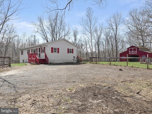 view of side of property featuring a barn, an outdoor structure, dirt driveway, and fence