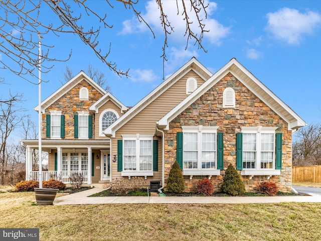 traditional-style home with stone siding, a front yard, and covered porch