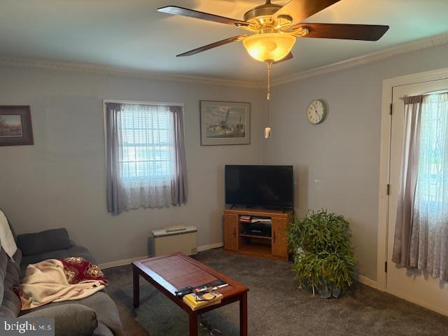 living room with ceiling fan, ornamental molding, dark carpet, and baseboards