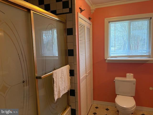 bathroom featuring ornamental molding, a closet, a shower with door, and baseboards