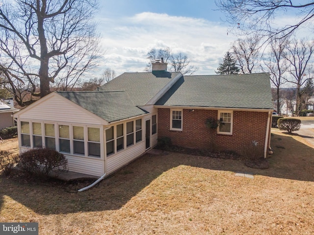 back of house with a shingled roof, a sunroom, brick siding, and a chimney