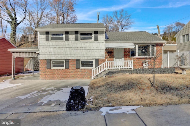 split level home featuring concrete driveway, brick siding, a shingled roof, and fence