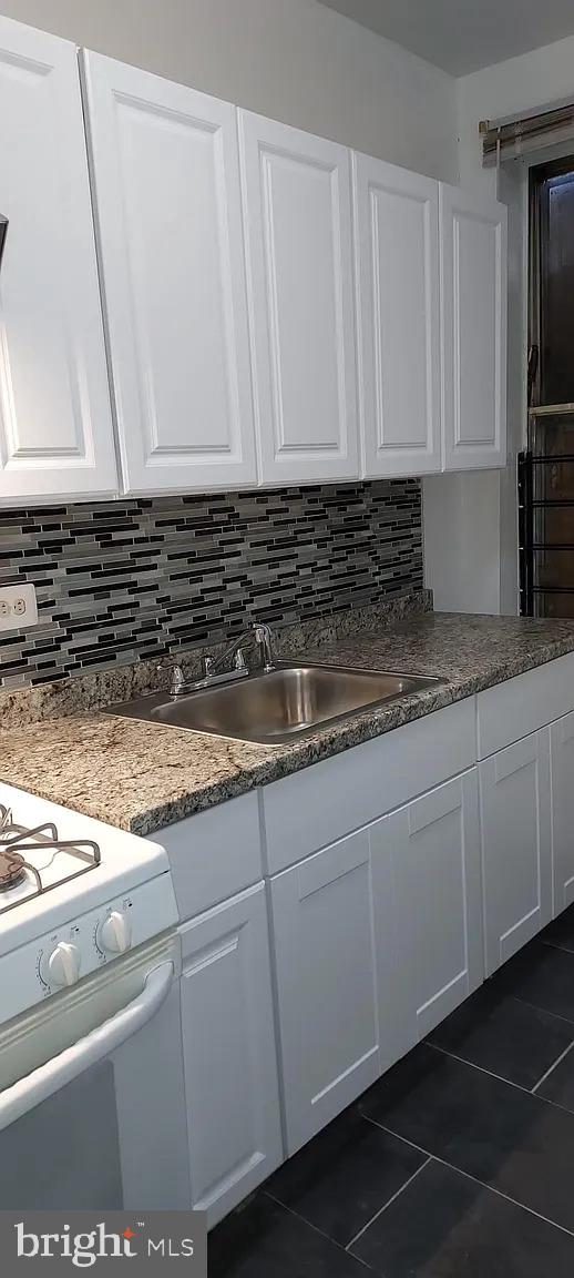 kitchen featuring tasteful backsplash, a sink, white cabinetry, and white range with gas cooktop