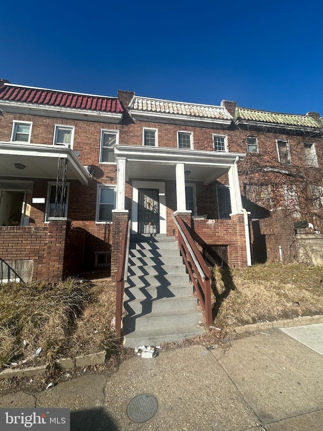 townhome / multi-family property with brick siding, stairway, a porch, and a tile roof