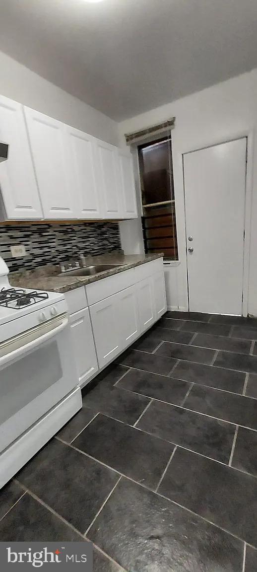 kitchen featuring dark countertops, white cabinets, white range with gas cooktop, and decorative backsplash