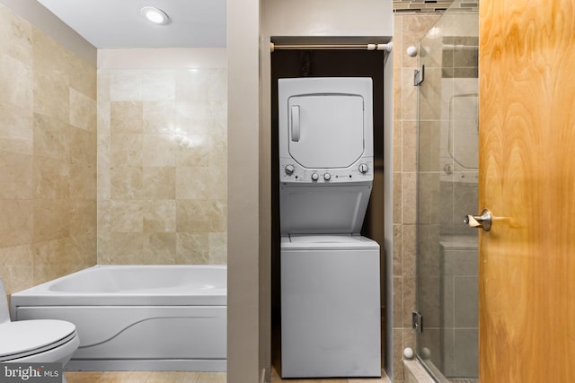 bathroom featuring walk in shower, toilet, stacked washer and clothes dryer, a bath, and tile patterned floors