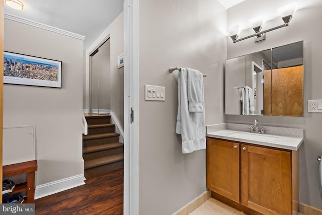 bathroom with vanity, crown molding, wood finished floors, and baseboards