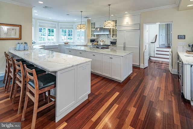 kitchen with glass insert cabinets, a peninsula, light stone countertops, white cabinetry, and pendant lighting