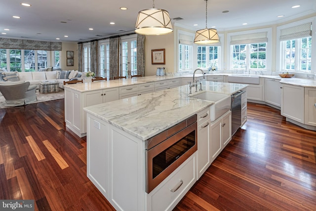 kitchen featuring light stone counters, a spacious island, a sink, appliances with stainless steel finishes, and decorative light fixtures