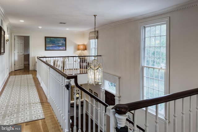 hallway featuring crown molding, light wood finished floors, visible vents, an inviting chandelier, and an upstairs landing