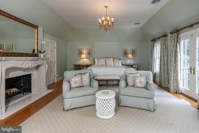 bedroom featuring lofted ceiling, an inviting chandelier, light wood-style flooring, and a high end fireplace