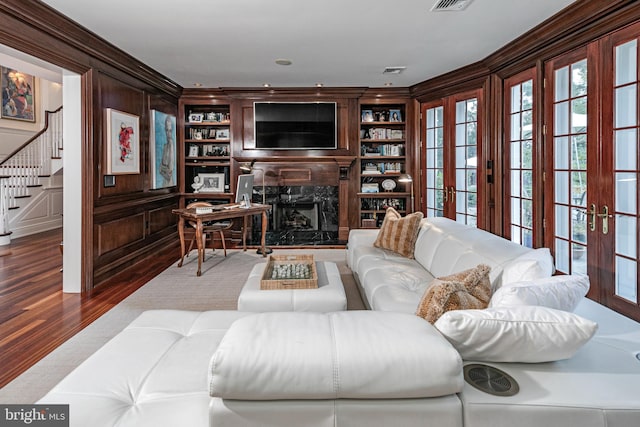 living area featuring french doors, a fireplace, wood finished floors, and built in features