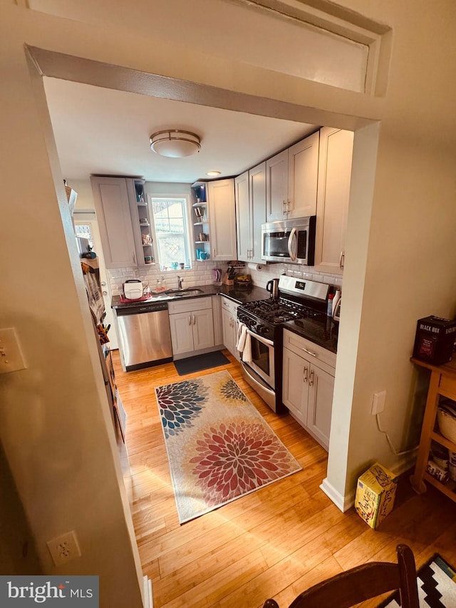 kitchen with dark countertops, open shelves, appliances with stainless steel finishes, and a sink