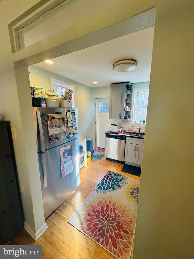 kitchen with backsplash, open shelves, light wood-type flooring, appliances with stainless steel finishes, and a sink