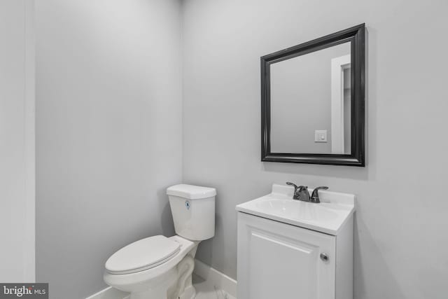 half bathroom with toilet, vanity, and baseboards