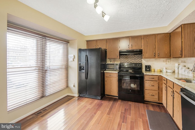 kitchen with tasteful backsplash, visible vents, wood finished floors, under cabinet range hood, and black appliances