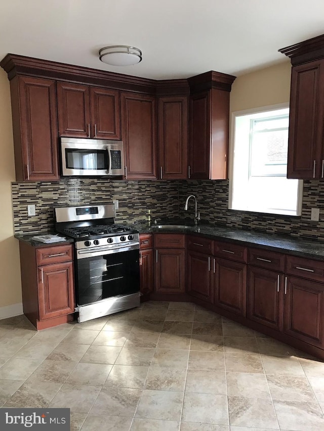 kitchen featuring appliances with stainless steel finishes, dark stone countertops, a sink, and decorative backsplash