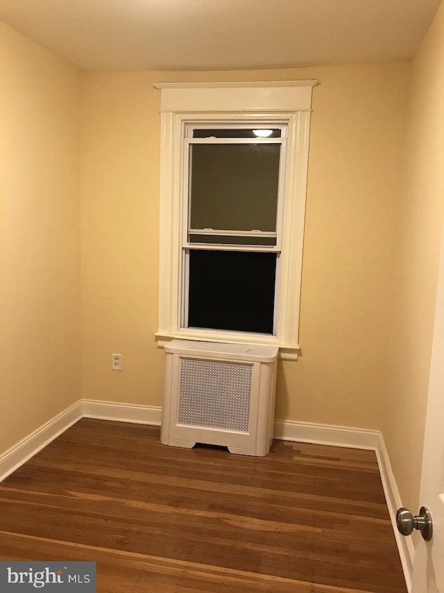 spare room featuring radiator, baseboards, and dark wood-type flooring