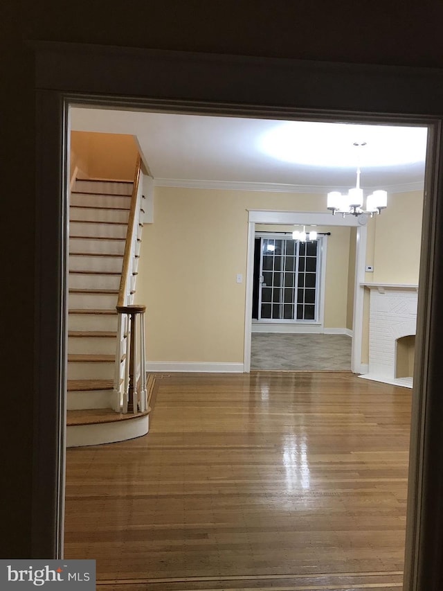 spare room with stairs, ornamental molding, a notable chandelier, and wood finished floors