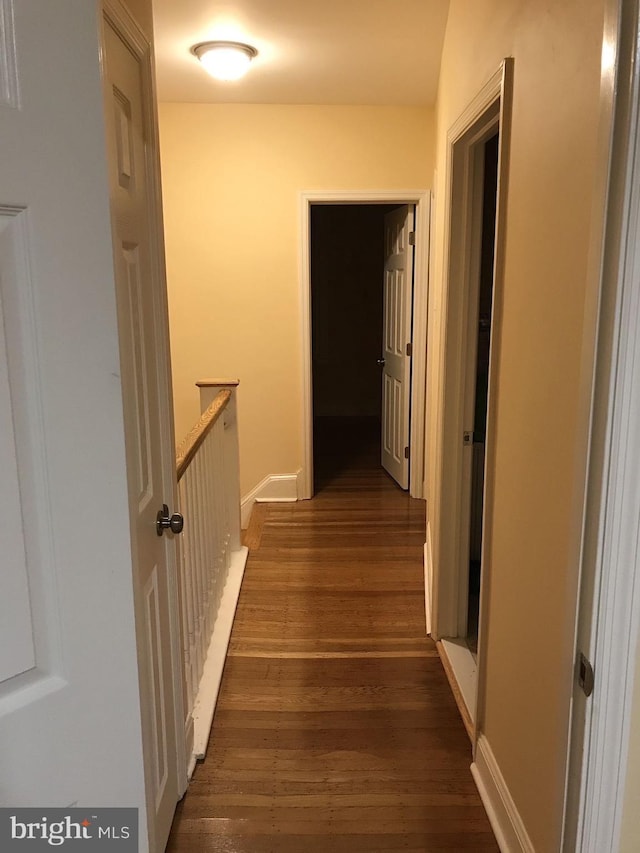 corridor featuring baseboards and dark wood-type flooring