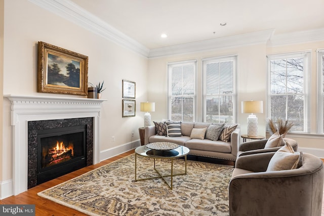 living room featuring baseboards, a glass covered fireplace, ornamental molding, wood finished floors, and recessed lighting