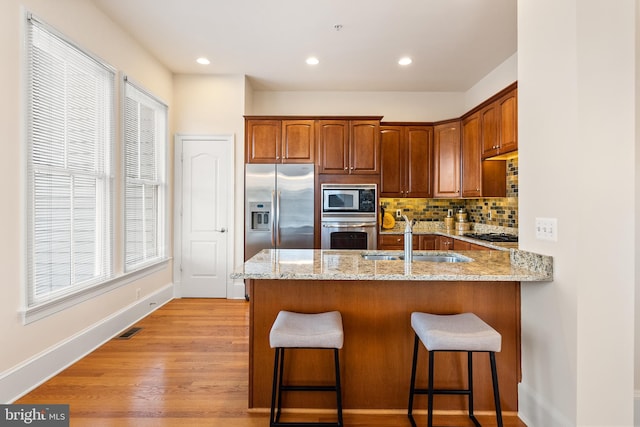 kitchen with light stone counters, a peninsula, a sink, visible vents, and appliances with stainless steel finishes