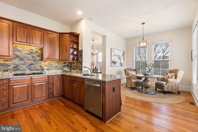 kitchen with brown cabinets, stainless steel appliances, hanging light fixtures, a sink, and a peninsula