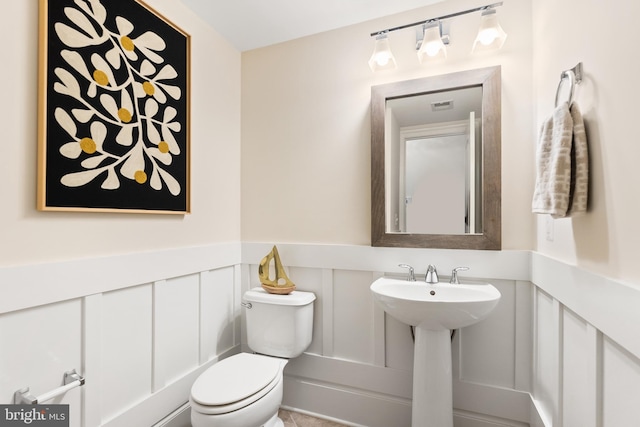 bathroom with wainscoting, visible vents, a decorative wall, and toilet