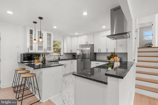 kitchen featuring decorative light fixtures, island exhaust hood, white cabinetry, stainless steel fridge, and a peninsula