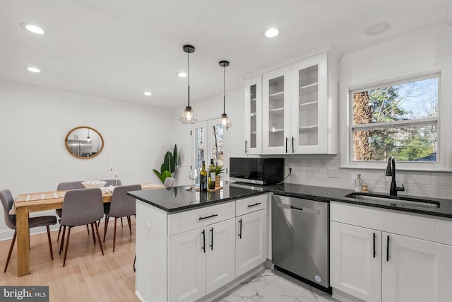 kitchen with dark stone counters, a sink, white cabinets, dishwasher, and decorative light fixtures