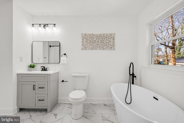 bathroom featuring marble finish floor, a soaking tub, toilet, and baseboards