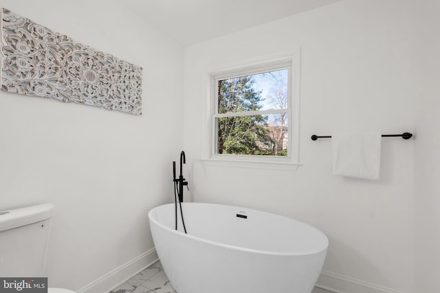 bathroom featuring toilet, marble finish floor, baseboards, and a freestanding bath