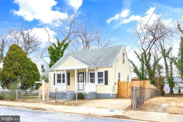 bungalow-style home with a fenced front yard, a porch, and a shingled roof