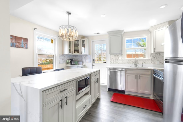 kitchen with white cabinets, glass insert cabinets, hanging light fixtures, stainless steel appliances, and a sink