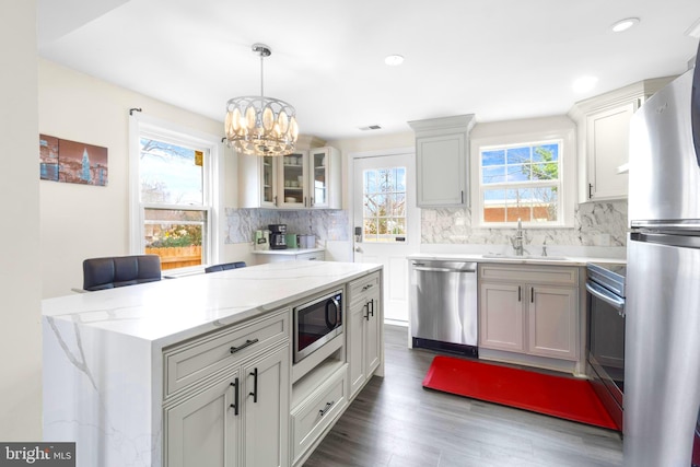 kitchen with stainless steel appliances, hanging light fixtures, glass insert cabinets, white cabinets, and a sink