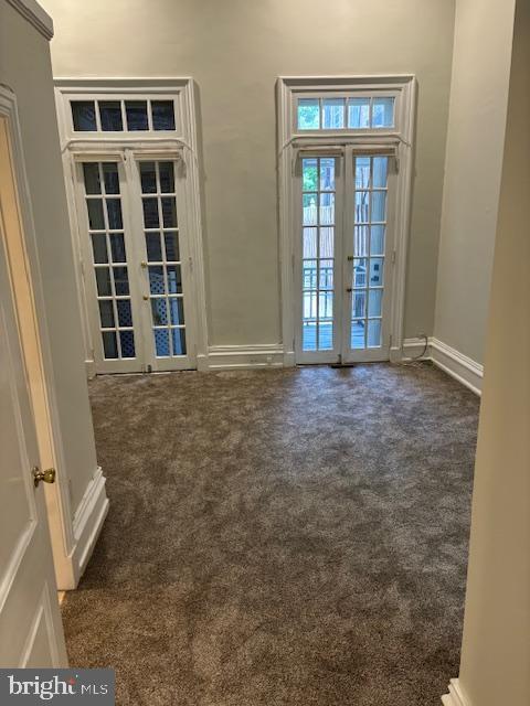 empty room with french doors, dark carpet, and baseboards