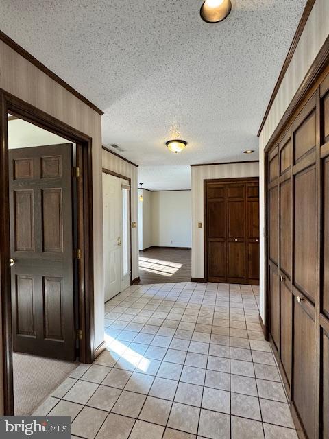 corridor featuring wooden walls, ornamental molding, a textured ceiling, and light tile patterned flooring