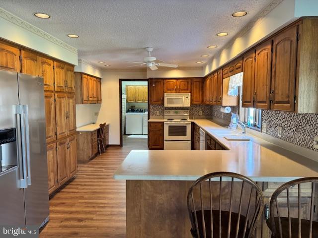 kitchen featuring a peninsula, white appliances, washer and clothes dryer, and light countertops