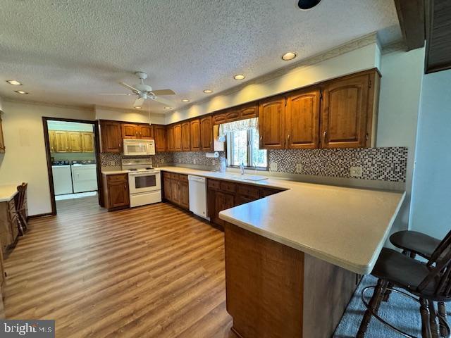 kitchen featuring a peninsula, white appliances, washer and dryer, light countertops, and brown cabinets