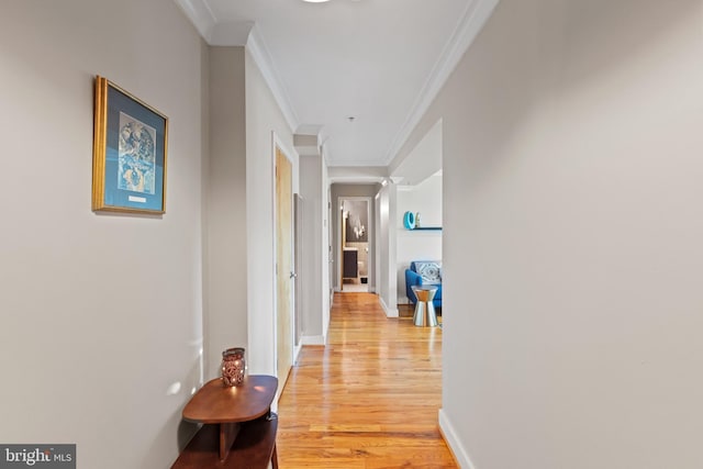 hallway featuring baseboards, light wood-style flooring, and crown molding