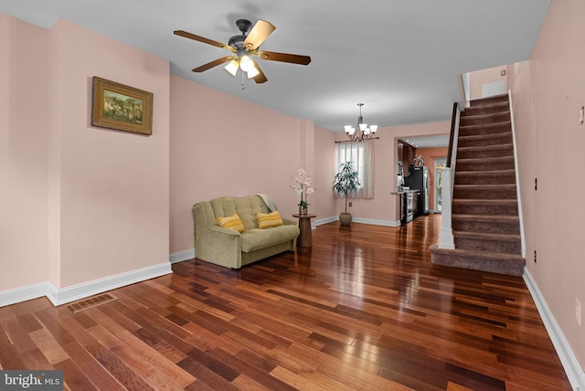 sitting room with stairs, dark wood-style flooring, visible vents, baseboards, and ceiling fan with notable chandelier