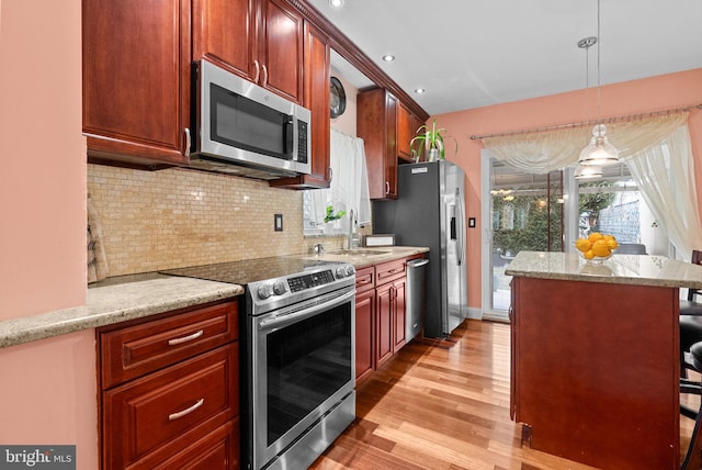 kitchen with light stone counters, a breakfast bar, pendant lighting, appliances with stainless steel finishes, and a sink