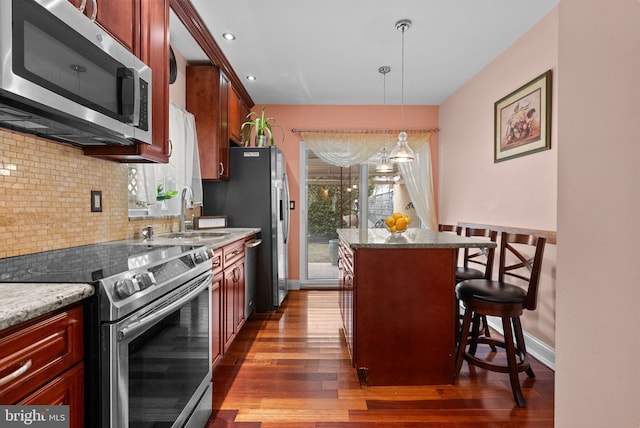 kitchen with appliances with stainless steel finishes, a center island, decorative light fixtures, a kitchen bar, and a sink