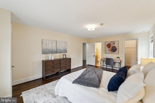 bedroom with ensuite bathroom, a spacious closet, dark wood-style flooring, and baseboards