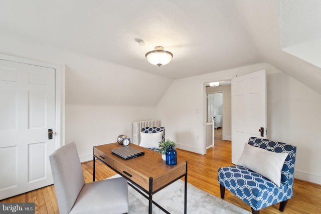 home office featuring vaulted ceiling, baseboards, light wood-style flooring, and radiator