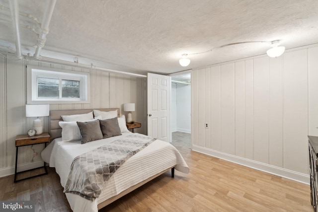 bedroom featuring light wood-type flooring, a textured ceiling, and baseboards